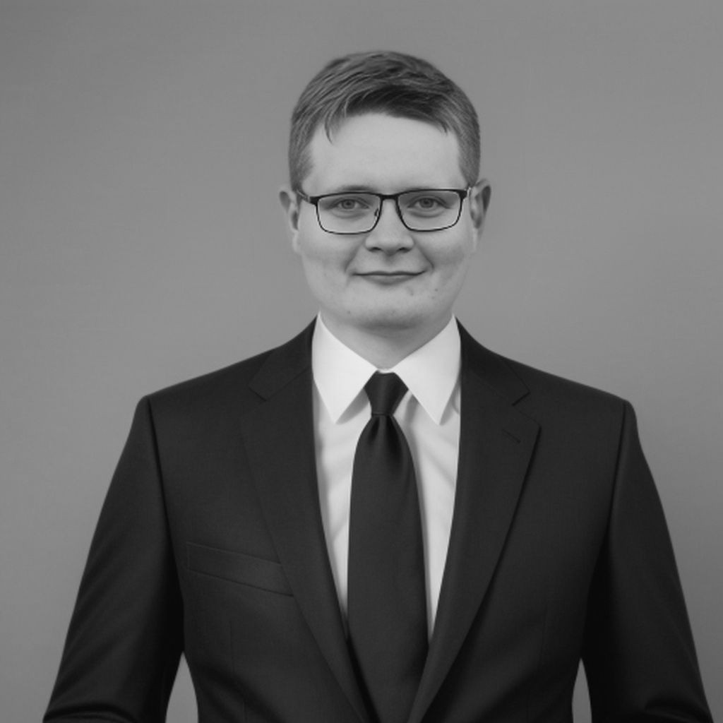 Black and white portrait of a person in a suit and tie with glasses, smiling.