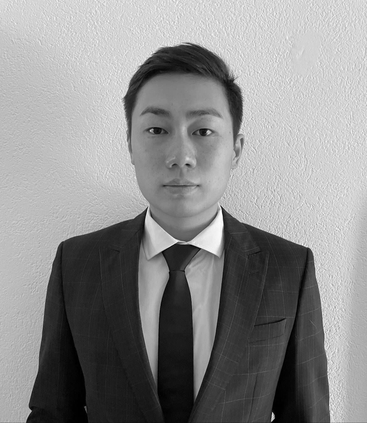 Black and white portrait of a person in a suit and tie against a textured wall.